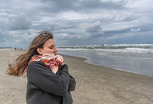 Frau an der Wasserkante am Strand von Juist im Herbst oder Winter