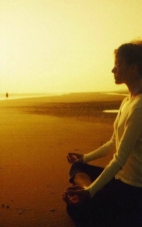 Eine Person meditiert und macht Yoga am Strand von Juist bei Sonnenuntergang