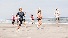 Ausdauertraining am Juister Strand mit dem Team des Strandsports, Menschen laufen an der Wasserkante mit hohen Schritten - Knie an die Ellbogen
