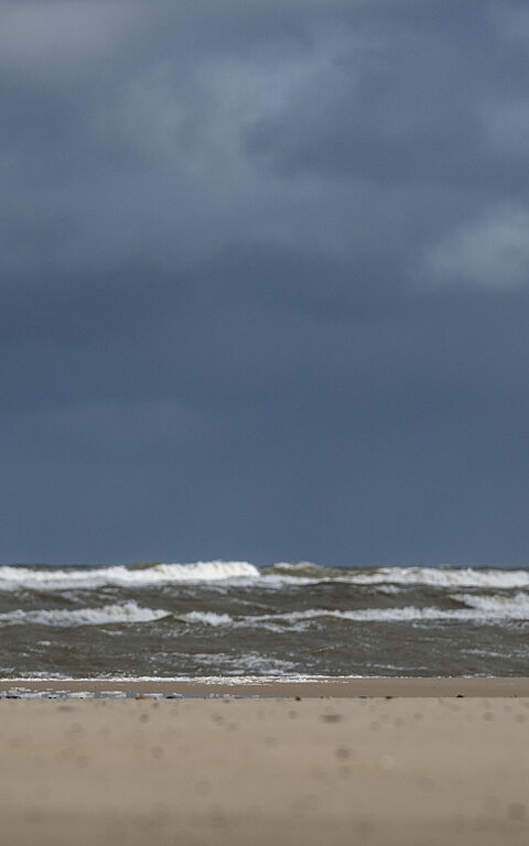 Person im Regenmantel am Juister Strand direkt an der Wasserkante spürt die Thalasso-Wirkung