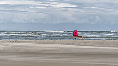 Person auf einer Bank am Strand auf Juist direkt an der Wasserkante im Herbst oder Winter