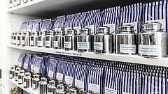 Echten Ostfriesentee auf Juist kaufen, zu sehen ist ein Regal mit den typisch blau-weiß gestreiften Teepackungen mit silbernen Gefäßen vor ihnen