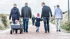 Familie geht auf der Juister Strandpromenade spazieren, Blick von hinten auf die Rücken der Spaziergänger, Oma, Opa, Eltern und zwei kleine Mädchen
