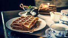 Eine traditionelle Auszeit bei Waffeln und Tee auf Juist genießen - blick auf eine Waffel im Zentrum des Bildes, daneben ostfriesisches Teegeschitt