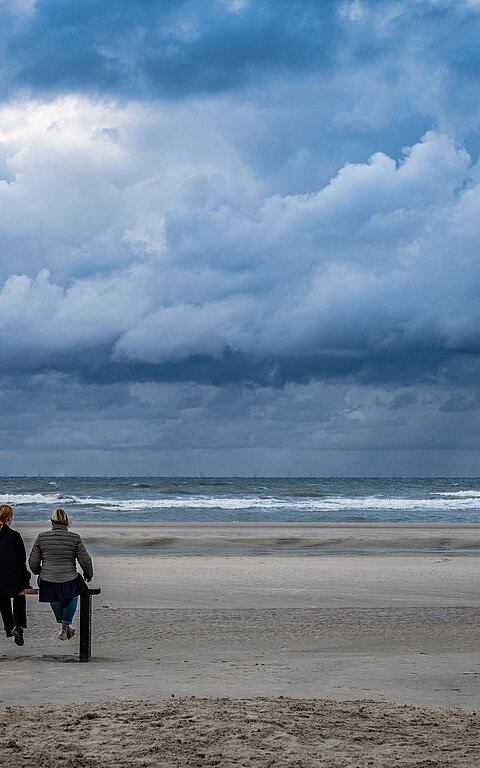 Wasserkante der Nordsee auf Juist mit Bank und zwei Personen auf der Bank