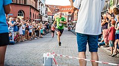 Läufer beim Insellauf, einem Wettkampf auf Juist, beim Zieleinlauf im Hintergrund, Mann mit weißem Shirt mit Aufschrift "Strandsport" im Vordergrund